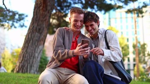Gay Couple Laughing Together Using a Smartphone in a Park