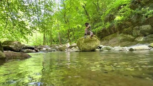 entspanne dich in der Natur, ein Mann sitzt auf einem großen Steinfelsen am Flussufer, Meditation, gesundes Leben, sauberer Naturwald