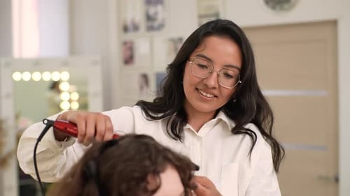 Closeup Portrait of Smiling Female Hairstylist Using Hair Iron and Comb for Unrecognizable Woman