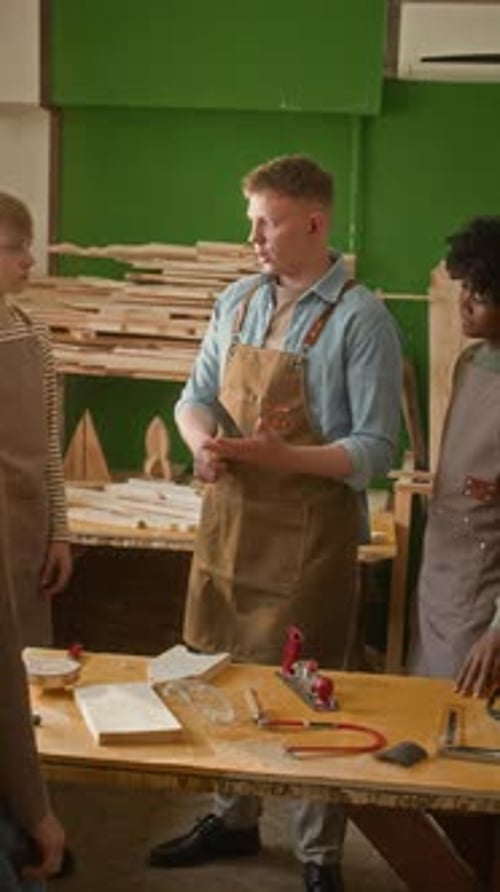 Vertical of Young Carpenter Teaching Diverse Kids to Use Hammer and Handplane