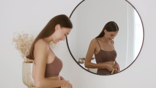 Jeune dame en pleine forme regardant un miroir, mesurant sa taille avec du ruban adhésif, souriant à son reflet