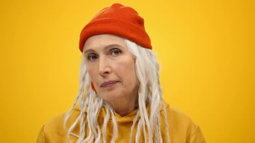 Mature woman grimacing and rolling eyes on yellow studio background indoors