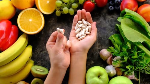 Hands Holding Supplements Surrounded by Fresh Fruits and Vegetables