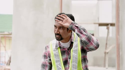Man wearing green reflective vest Taking off helmet to cool off After working on construction site.