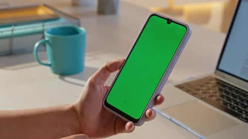 Woman Using Smartphone with Green Screen at Desk