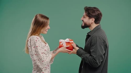 Young Couple On Green Background Blonde Woman Gives Gift With Bow To Boyfriend
