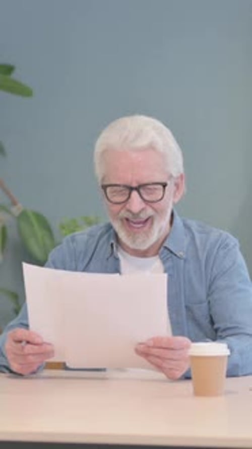 Senior Man Reads Documents and Reacts Positively Indoors
