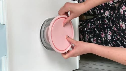 A Woman Examines Glass Food Containers With Plastic Lids. Reviews The Purchase