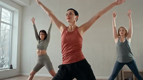 Three Women Practicing Yoga in Bright Room with Large Windows