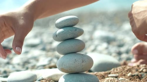 Woman Hand Building Pebbles Tower On Beach During Holidays. Macro Of Human Hand Making Tower From...
