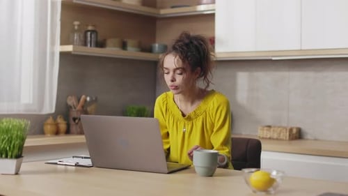 Young Woman Working on Laptop at Kitchen Table