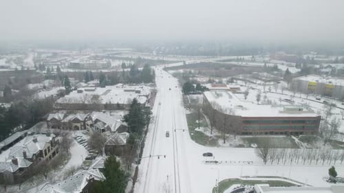 A drone shot captures a snowy road with passing cars, rising upward into a cloud-covered, endless st