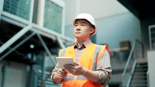 Professional engineer wearing safety helmet and vest standing at the factory and working