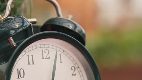 Reloj antiguo negro de cerca, de estilo clásico, que muestra minutos después de las tres sobre un fondo borroso, inclinado hacia abajo