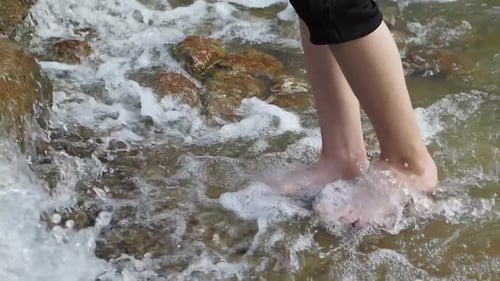 Boy with Bare Feet Carefully Crossing Over a Small Stream From a Waterfall