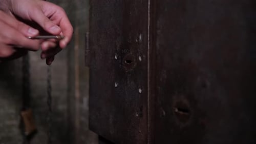 A Man's Hand Opens an Old Rusty Metal Door with an Antique Key in a Dark Room