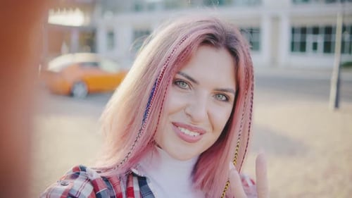 Beautiful Young Hipster Woman with Pink Hair Takes a Selfie in the Park or on the Street at Sunset