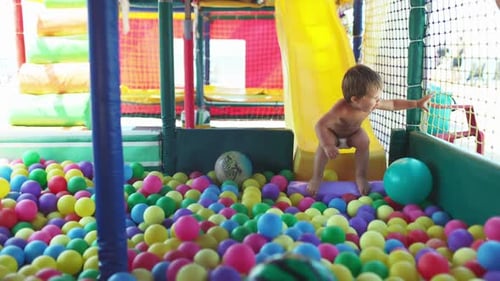 L'enfant joue dans la salle de jeux et descend le toboggan dans la piscine avec de petites balles