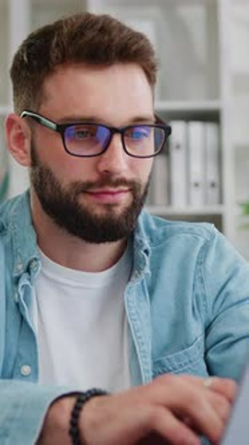 Man with Glasses Typing on Laptop in Office