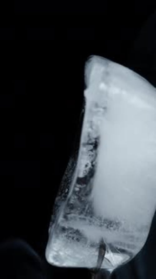 An ice cube rotates on a black background, emitting smoke, in a close-up shot. Isolate