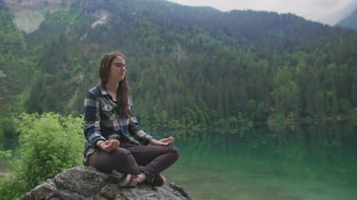 Wide shot of a Woman doing Yoga and Meditation on a rock surrounded by Nature in a Mountain Lake loc