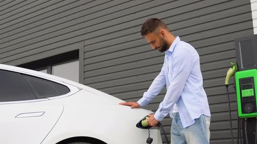 A Man Unplugs Charging Cable Electric Vehicle at Station Green Energy Eco Friendly Fuel
