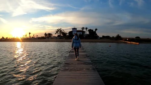 Young woman walking through a wooden pier bridge by the beach at sunset. Summertime concept.