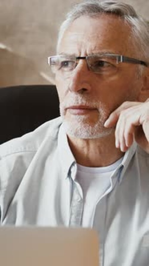 Mature Businessman is Looking Thoughtful Sitting at Desk and Typing on His Laptop While Working at