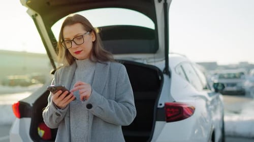 Woman Uses Phone Next to Car Trunk