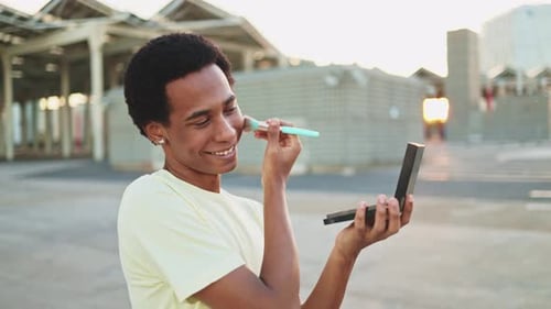 Afro non-binary person applying make-up outdoors.