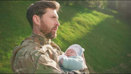 In the Park Serious Happy Soldier in Uniform is Hugging Kissing His Newborn Daughter Outdoors Stand