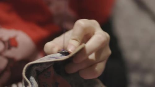 Hands Sew Button on Material with Needle and Thread