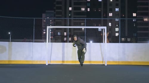 Goalkeeper Rolling Soccer Ball on Urban Field at Night