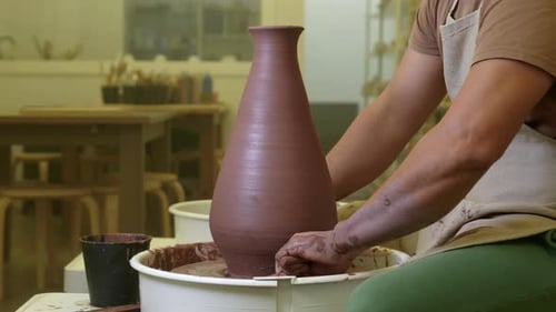 Potter carefully cutting completed vase with thread on workshop pottery wheel