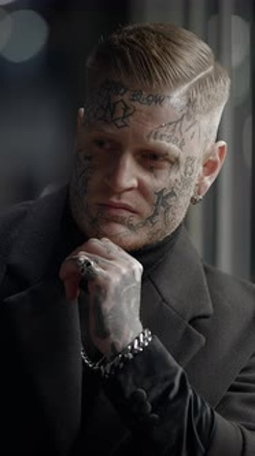 Tattooed Man Stares Thoughtfully Out of Window at Night