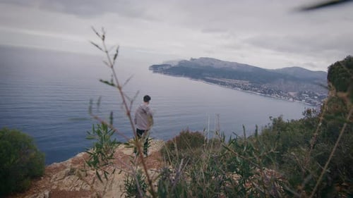 Male tourist standing on cliff at Mediterranean Sea coast admiring scenic view