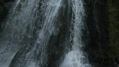 Close-up of waterfall streaming over moss-covered rock face, filmed in ultra slow motion with a