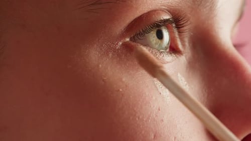Junge grünäugige Frau, die beige Foundation auf ihr Gesicht aufträgt, Nahaufnahme, Makro-Schönheits-Hautpflege-Make-up