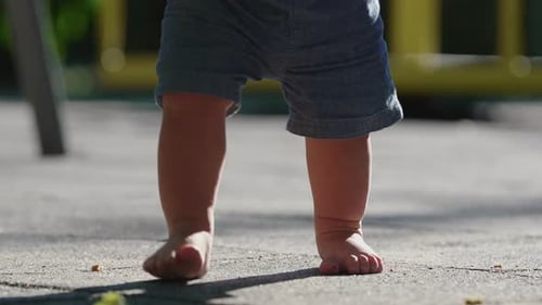 Barefoot toddler walking on playground surface with small careful steps capturing balance