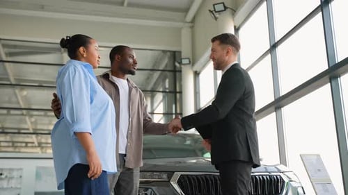 Happy Couple Shaking Hands with Car Salesman in Dealership