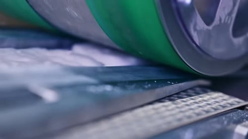 Huge heavy green shaft rotating slowly over the conveyor. Diaper production enterprise in blur.