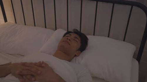 Asian attractive man lying down on bed in bedroom, dreaming at night.