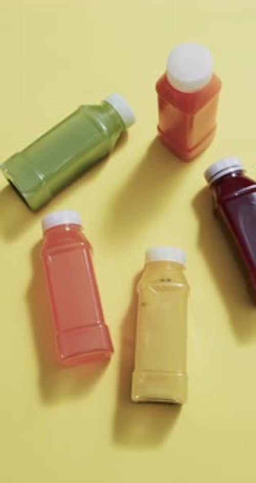 Vertical video of bottles of fruit juice with copy space over yellow background