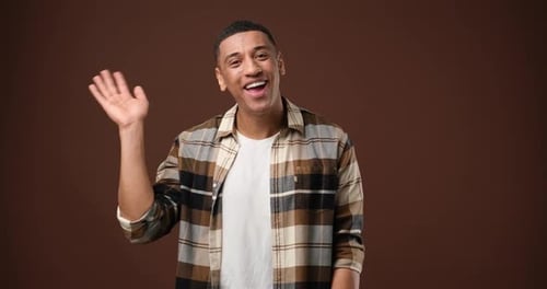 Smiling Man Waving Hello on Brown Background