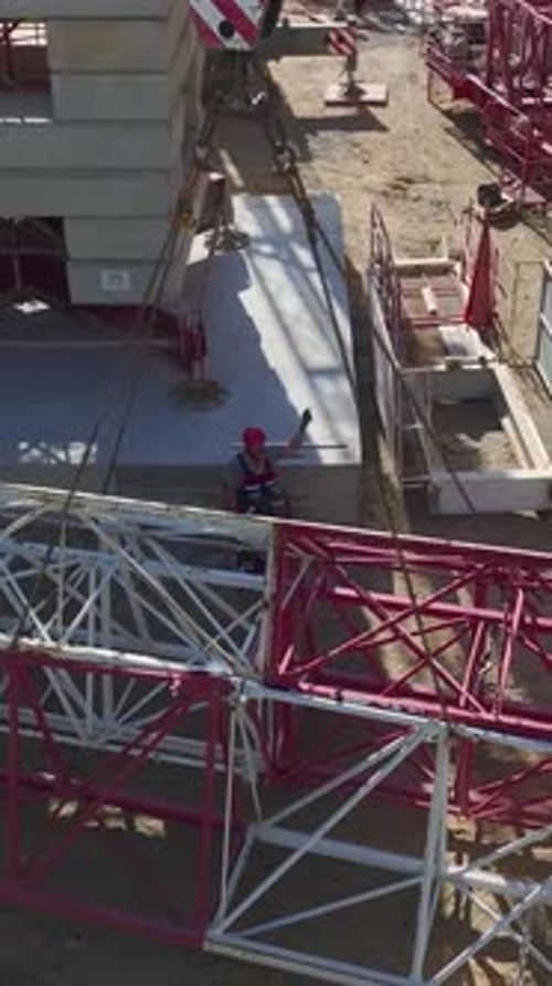 Vertical Video Construction Workers Joining Parts Of A Tower Crane OnSite Captured Aerially With