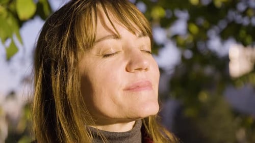 An Attractive Middleaged Caucasian Woman Smiles with Her Eyes Closed in a Park Closeup