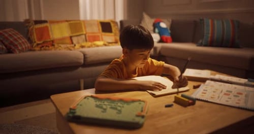 Portrait of a Cute Little Korean Boy Thinking and Writing in his Notebook in a Living Room During E