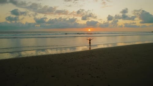 Person stands on beach at sunset watching ocean horizon under colorful sky