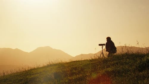 Der Fotograf fotografiert die Natur bei Sonnenaufgang mit einem großen Teleobjektiv mit Bergen auf dem