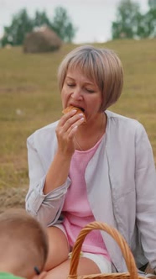 Mother Enjoying Fish Roll with Children and Aunt in Open Field During Picnic
